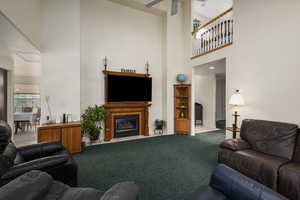 Carpeted living area featuring baseboards, a high ceiling, a fireplace with flush hearth, and ceiling fan