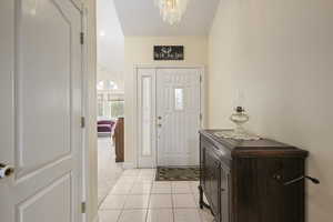 Entrance foyer with light colored carpet, baseboards, light tile patterned flooring, and a notable chandelier