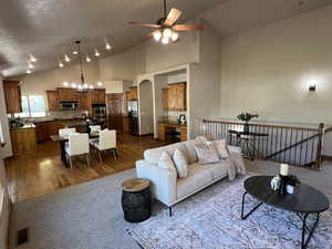 Living room featuring visible vents, dark carpet, high vaulted ceiling, dark wood finished floors, and ceiling fan with notable chandelier