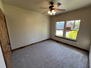 Spare room with a textured ceiling, ceiling fan, light colored carpet, and baseboards