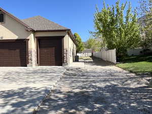 View of property exterior featuring a garage, fence, stone siding, stucco siding, and driveway