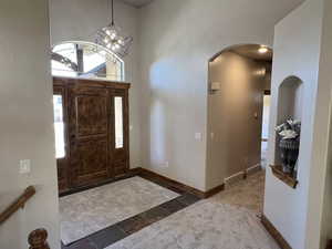 Carpeted entrance foyer with baseboards, arched walkways, and an inviting chandelier