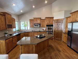 Kitchen featuring high vaulted ceiling, dark wood-type flooring, brown cabinets, a sink, and stainless steel appliances