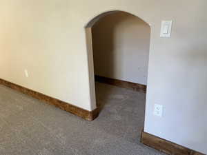 Empty room featuring carpet floors, arched walkways, and baseboards