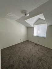 Bonus room featuring a textured ceiling, visible vents, vaulted ceiling, carpet floors, and baseboards
