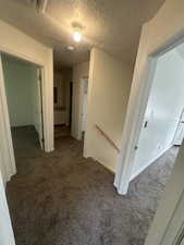 Hallway with carpet, a textured ceiling, and an upstairs landing