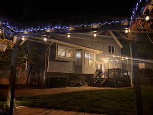 Back of house at night featuring a lawn, stairs, and a wooden deck