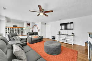 Living room featuring a ceiling fan, a textured ceiling, a fireplace, light wood finished floors, and stairs
