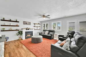 Living room featuring a textured ceiling, ceiling fan, visible vents, and light wood-style floors