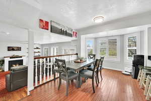 Dining area with a warm lit fireplace, a textured ceiling, and light wood-style flooring