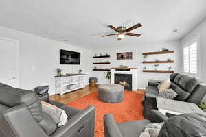 Living area with visible vents, a textured ceiling, a ceiling fan, wood finished floors, and a lit fireplace