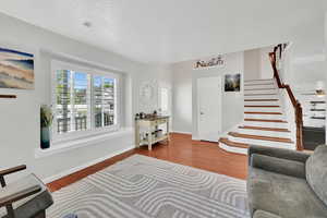 Living area featuring baseboards, a textured ceiling, wood finished floors, and stairway