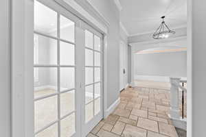 Corridor with an inviting chandelier, baseboards, ornamental molding, and stone tile floors
