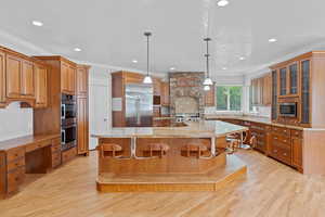 Kitchen featuring crown molding, built in appliances, brown cabinets, a large island with sink, and a sink