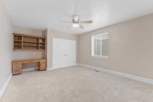 Unfurnished bedroom with ceiling fan, light carpet, built in desk, baseboards, and a closet