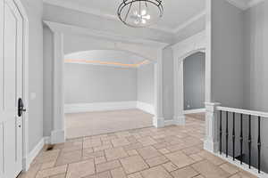 Entryway featuring crown molding, arched walkways, a chandelier, stone finish floor, and visible vents
