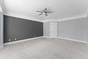 Carpeted empty room featuring crown molding, baseboards, and ceiling fan