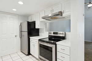 Kitchen with under cabinet range hood, stainless steel appliances, white cabinetry, and light countertops