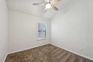Empty room with carpet floors, baseboards, ceiling fan, and vaulted ceiling