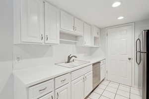 Kitchen featuring appliances with stainless steel finishes, a sink, light countertops, white cabinets, and recessed lighting