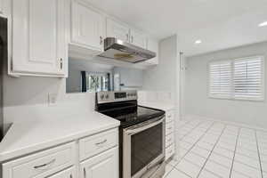 Kitchen with recessed lighting, white cabinetry, under cabinet range hood, light tile patterned floors, and stainless steel range with electric cooktop