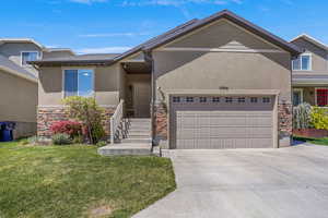 View of front facade featuring a front yard, stone siding, stucco siding, an attached garage, and driveway