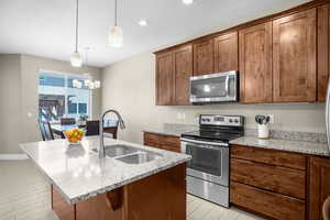 Kitchen with light stone counters, a sink, a chandelier, an island with sink, and stainless steel appliances