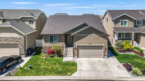 Craftsman inspired home featuring driveway, a front yard, an attached garage, stone siding, and stucco siding