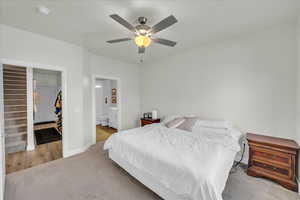 Carpeted bedroom with baseboards, a ceiling fan, ensuite bathroom, and a spacious closet