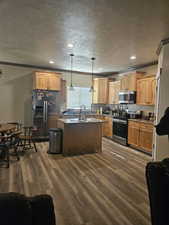 Kitchen with ornamental molding, a kitchen island, dark wood-style floors, a textured ceiling, and stainless steel appliances