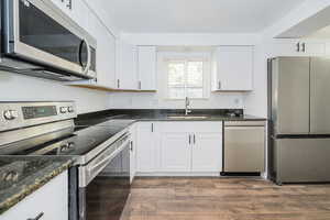 Kitchen with dark wood-style floors, white cabinets, a sink, dark stone countertops, and appliances with stainless steel finishes