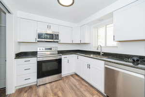 Kitchen featuring dark wood-style flooring, white cabinets, a sink, dark stone countertops, and appliances with stainless steel finishes