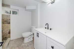 Bathroom with vanity, toilet, stone tile floors, baseboards, and tiled shower
