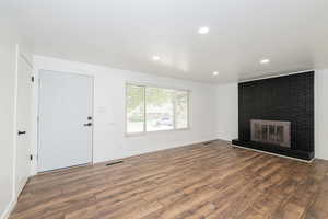 Unfurnished living room with visible vents, baseboards, a brick fireplace, and wood finished floors