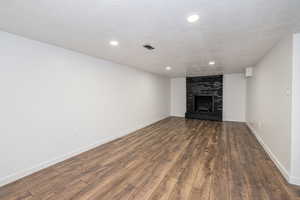 Unfurnished living room featuring a brick fireplace, recessed lighting, a textured ceiling, and dark wood-type flooring