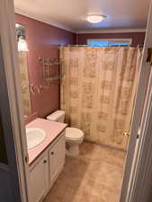 Full bathroom featuring a shower with curtain, a textured ceiling, vanity, toilet, and ornamental molding