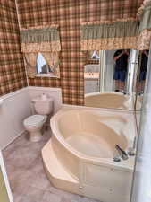 Full bathroom featuring toilet, tile patterned floors, a wainscoted wall, wallpapered walls, and a bath