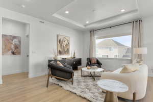 Sitting room with baseboards, a tray ceiling, wood finished floors, and visible vents