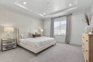 Bedroom with baseboards, recessed lighting, a tray ceiling, and light colored carpet