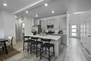 Kitchen with gray cabinets, a kitchen bar, visible vents, a center island with sink, and stainless steel appliances