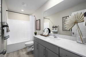 Bathroom featuring toilet, shower / bath combo with shower curtain, wood finished floors, and vanity