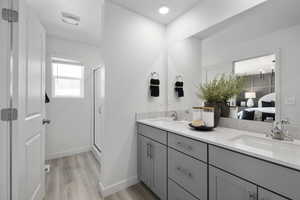 Ensuite bathroom with double vanity, a shower stall, a sink, and wood finished floors
