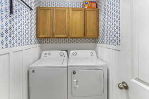 Laundry room featuring wainscoting, wallpapered walls, cabinet space, and washer and dryer