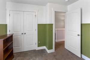 Unfurnished bedroom featuring carpet flooring, a closet, and a wainscoted wall