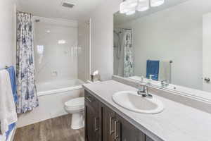 Bathroom featuring visible vents, wood finished floors, shower / tub combo, vanity, and toilet