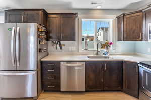 Kitchen featuring dark brown cabinetry, appliances with stainless steel finishes, a sink, light countertops, and visible vents