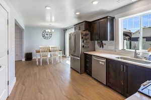 Kitchen with dark brown cabinets, a sink, light countertops, an inviting chandelier, and stainless steel appliances