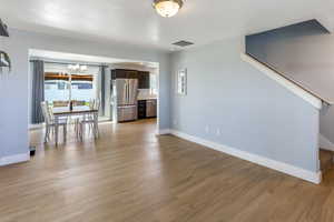 Unfurnished living room featuring visible vents, baseboards, a notable chandelier, light wood-style floors, and stairs