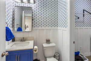 Bathroom with wainscoting, vanity, toilet, a decorative wall, and wallpapered walls
