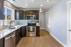 Kitchen with dark brown cabinetry, light wood-style floors, recessed lighting, a sink, and stainless steel appliances